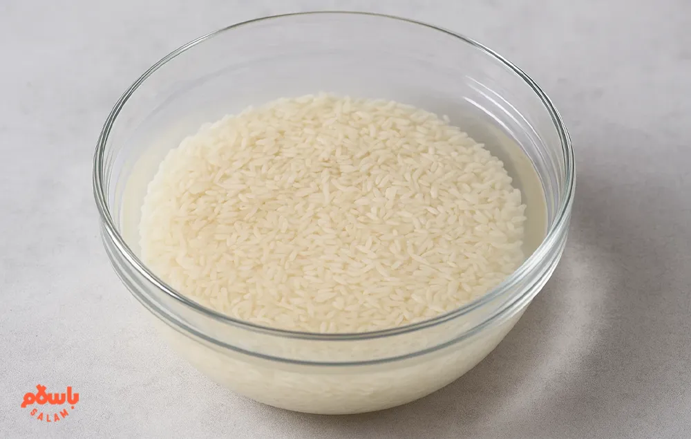 خیس کردن برنج خام کامفیروزی در کاسه شیشه‌ای شفاف