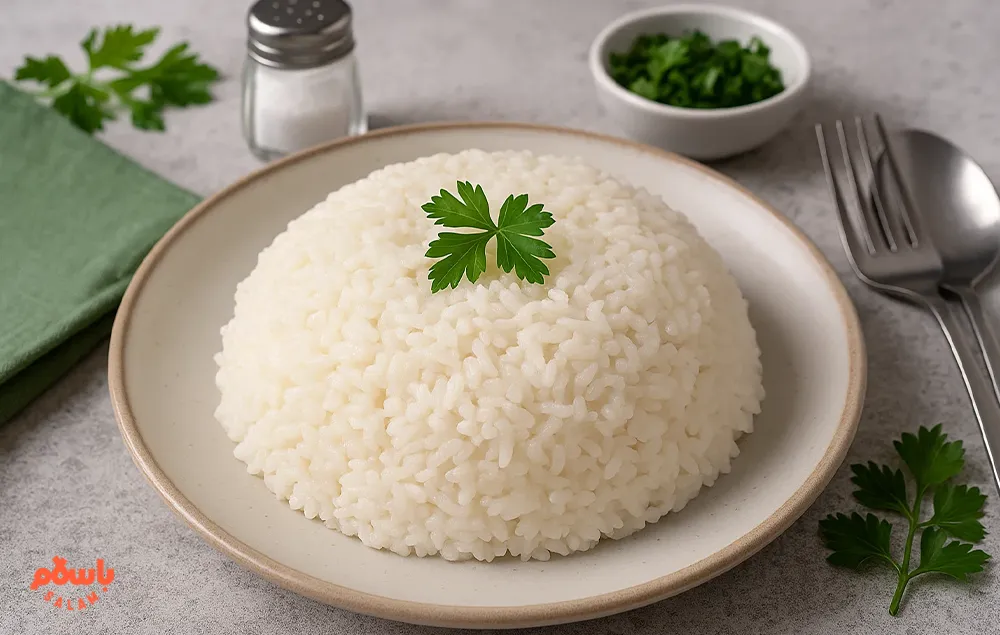 یک بشقاب برنج کامفیروزی کته تزئین‌شده با برگ جعفری، همراه با قاشق و چنگال روی میز سرو